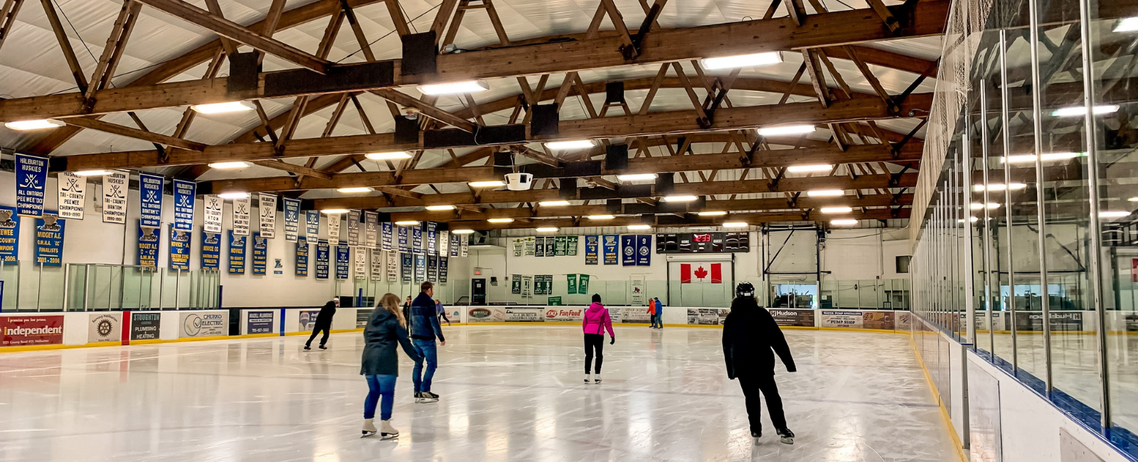 Shiny ice surface with wooden rafters on the ceiling and people skating.